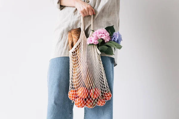 Жінка тримає торгову сумку з помідорами, хлібом та квітами. Концепція екології, охорони навколишнього середовища. Нульові відходи . Стокова Картинка