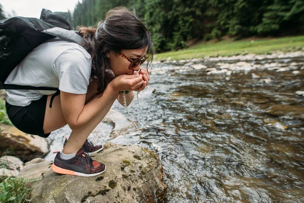 Chica viaja bebiendo agua de un río de montaña —  Fotos de Stock