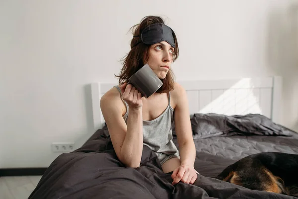 young woman feels bad sitting in bed with a cup of coffee