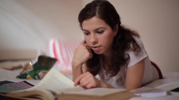 Student meisje lezen en eten in bed — Stockvideo