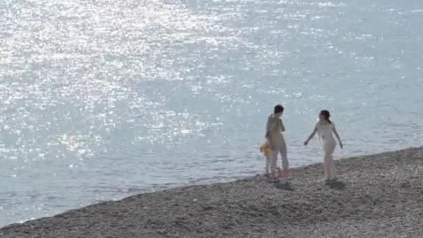 Boldog szülők és a lánya séta a tengerparton a napsütéses napon — Stock videók