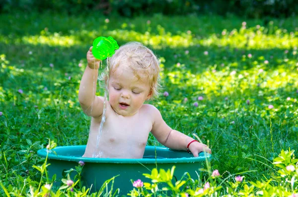 Yürümeye başlayan çocuk sokakta bir sıcak yaz gününde eğleniyor su ile mavi gözlü kız bebek.