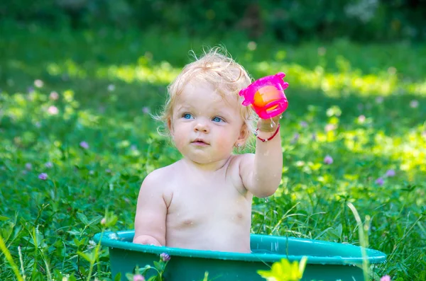 Yürümeye başlayan çocuk sokakta bir sıcak yaz gününde eğleniyor su ile mavi gözlü kız bebek.