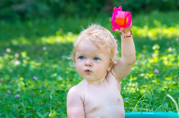 Yürümeye başlayan çocuk sokakta bir sıcak yaz gününde eğleniyor su ile mavi gözlü kız bebek.