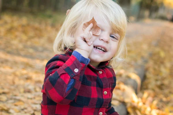 small girl with blue eyes covering one eye with a leaf