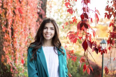 Uzun saçlı Genç güzel esmer kız kameraya doğru sonbahar ve yeşillik arka plan üzerinde görünüyor.