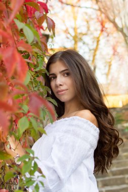 Uzun saçlı Genç güzel esmer kız kameraya doğru sonbahar ve yeşillik arka plan üzerinde görünüyor.