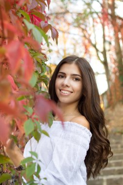 Uzun saçlı Genç güzel esmer kız kameraya doğru sonbahar ve yeşillik arka plan üzerinde görünüyor.