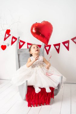 kalp şeklinde balon dekore edilmiş bir Sevgililer günü Studio ile beyaz elbiseli küçük kız