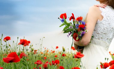 Bir buket taze kır çiçeği ve gelincikler bir kızın ellerinde.