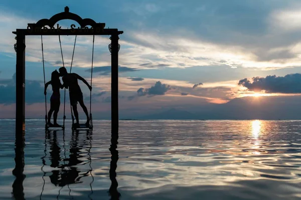 couple kissing on the Swing in the sea at the sunset