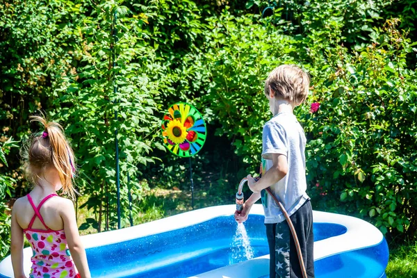 Menino e menina enchendo piscina com água — Fotografia de Stock