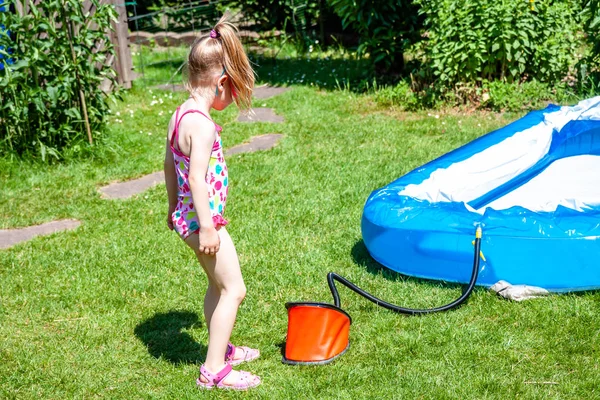 Little girl blowing up inflatable swimming pool