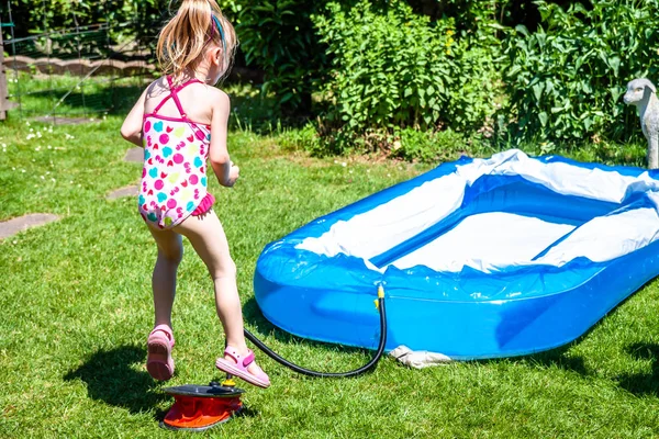 Lilla flickan hoppar på bälgen att spränga uppblåsbara poolen — Stockfoto