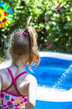 Little girl looking forward to jump into the inflatable swimming pool clipart