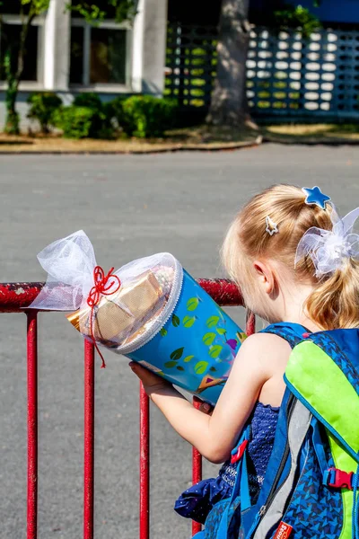 Niña parada frente al edificio de la escuela sosteniendo su cono de caramelo — Foto de Stock