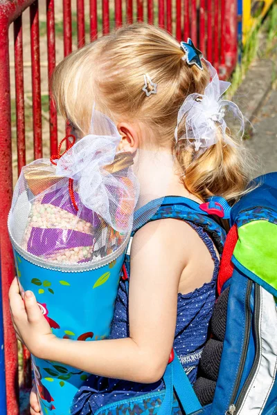Děvčátko stojí před školní budovy, drží ji bonbóny kužele — Stock fotografie