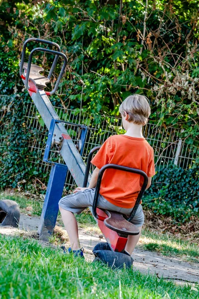 Pojke ensam spelar på den se-såg på lekplatsen — Stockfoto