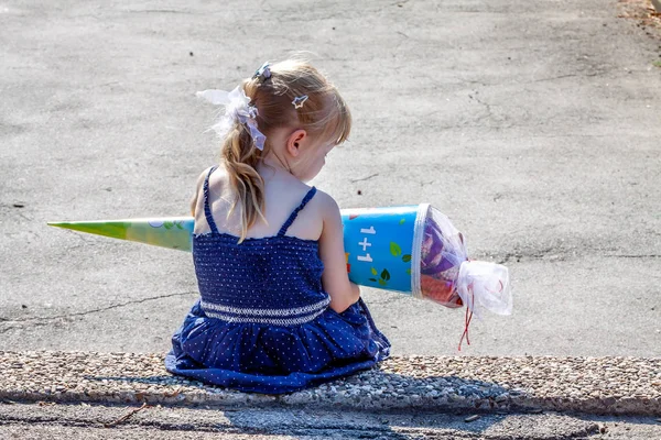 Malá holka sedí v přední části školní budovy, drží ji bonbóny kužele — Stock fotografie