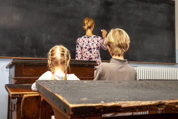 Concept of public primary school education with young boy and girl listening to the female teacher