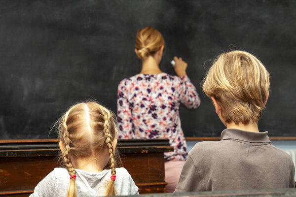 Concept of public primary school education with young boy and girl listening to the female teacher