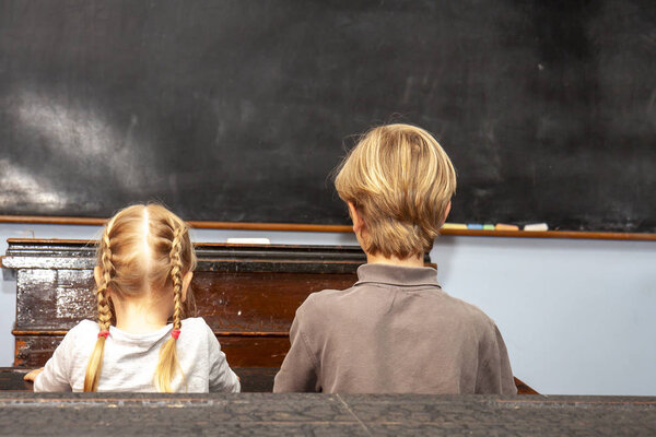 Concept of public primary school education with young boy and girl sitting in the classroom