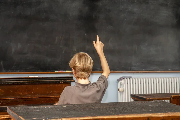 Konzept der öffentlichen Grundschulerziehung mit einem kleinen Jungen, der im Klassenzimmer die Hand hebt — Stockfoto