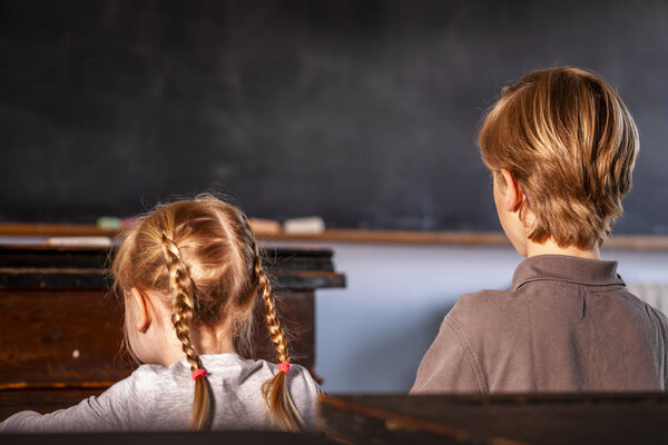 Concept of public primary school education with young boy and girl sitting in the classroom