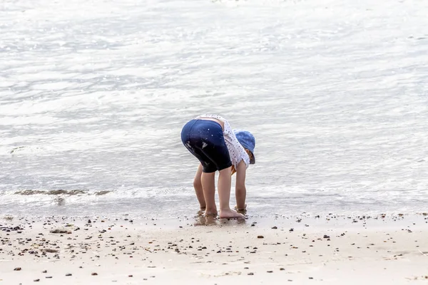 Маленька дівчинка грає на пляжі з мушлями — стокове фото