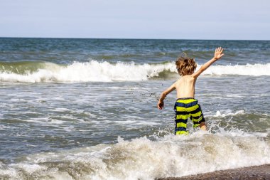 Küçük çocuk sahilde dalgaların içine çalışan
