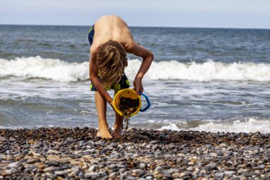 Taşlarla oynayan bir kova ile küçük çocuk ve kum plaj