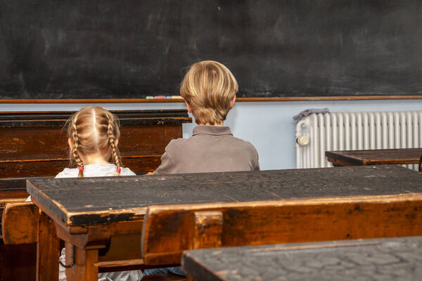 Concept of public primary school education with young boy and girl sitting in the classroom