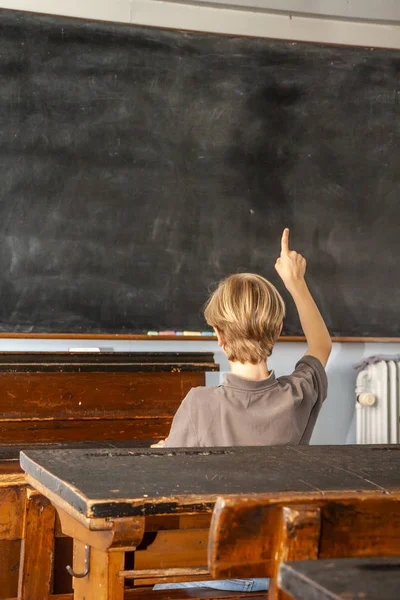 Concept of public primary school education with young boy raising his hand in the classroom — Stock Photo, Image