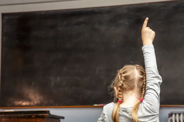 Konzept der öffentlichen Grundschulerziehung mit einem jungen Mädchen, das im Klassenzimmer die Hand hebt — Stockfoto