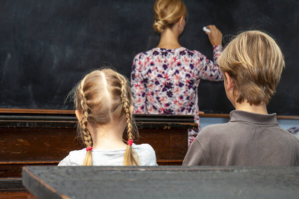 Concept of public primary school education with young boy and girl listening to the female teacher