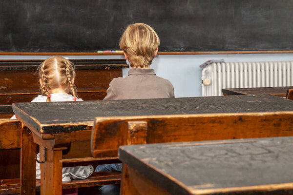 Concept of public primary school education with young boy and girl sitting in the classroom