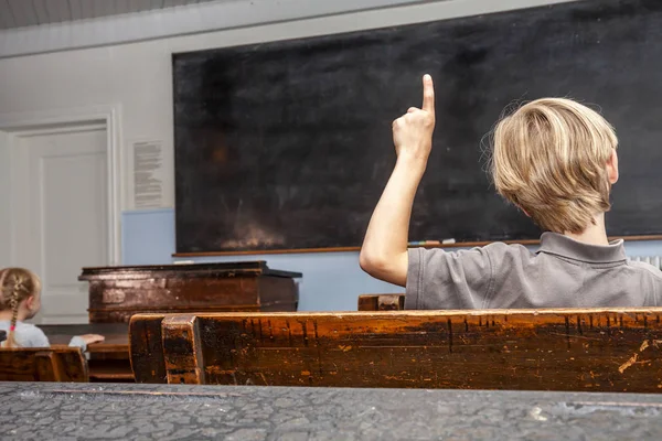 Concept d'enseignement primaire public avec un jeune garçon levant la main en classe — Photo