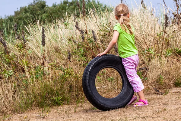 Liten flicka som leker med gamla används ruttna papperskorgen däck på torr sommar gräs — Stockfoto