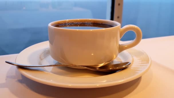 Tasse Kaffee mit Löffel auf einem Tisch mit dem Ozean im Hintergrund, während das Kreuzfahrtschiff fährt — Stockvideo
