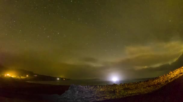 Timelapse of the sky above Staffin Bay on the Isle of Skye with stars, clouds, the milky way and aurora borelais coming in — стоковое видео