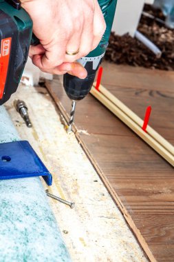 Evde yeni Ahşap laminat yüklerken matkap makinesi kullanan adam.