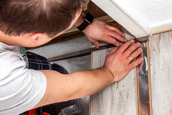 Homme utilisant coude mesure et crayon lors de l'installation de nouveaux planchers stratifiés en bois à la maison . — Photo