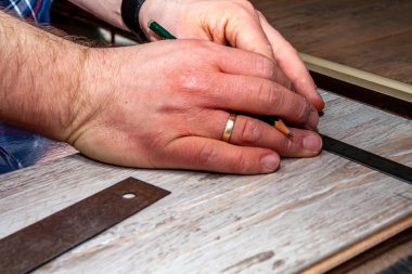Man using measuring elbow and pencil while installing new wooden laminate flooring at home. clipart