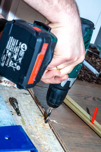 Man using drill machine while installing new wooden laminate flooring at home.