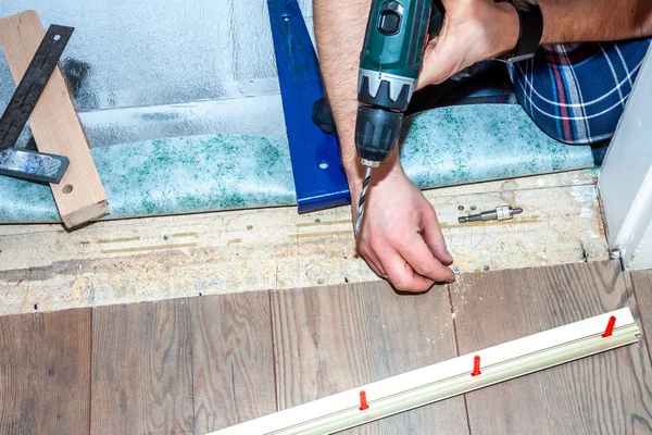 Homem usando máquina de broca durante a instalação de novo piso laminado de madeira em casa . — Fotografia de Stock