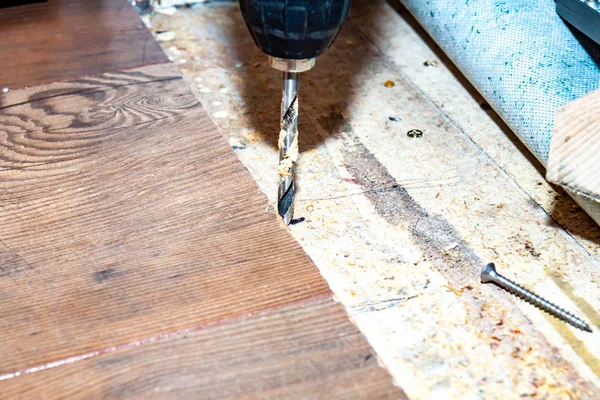 Man met behulp van boor machine tijdens het installeren van nieuwe houten laminaat vloeren thuis. — Stockfoto