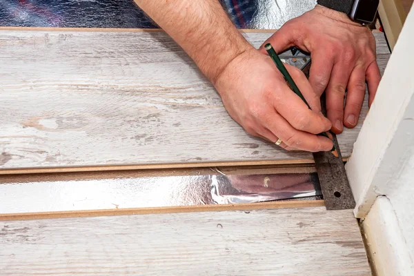 Homem usando cotovelo de medição e lápis durante a instalação de novo piso laminado de madeira em casa . — Fotografia de Stock