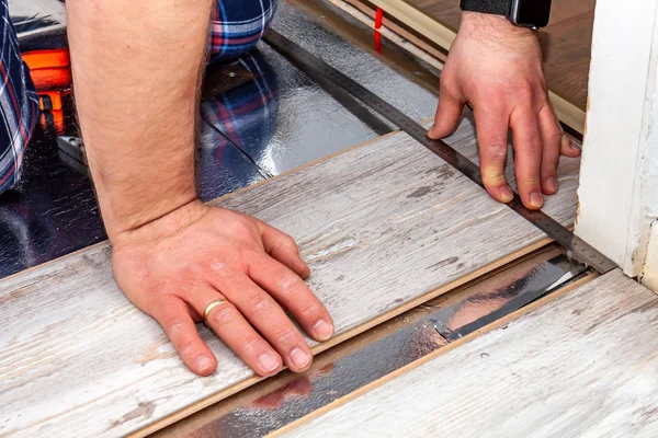 Man using measuring elbow and pencil while installing new wooden laminate flooring at home. — Stock Photo, Image