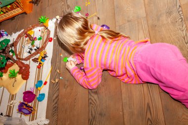 Renkli plastik oyuncak bir sürü ile kapalı ahşap zemin üzerinde oynayan küçük kız çocuk