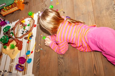 Renkli plastik oyuncak bir sürü ile kapalı ahşap zemin üzerinde oynayan küçük kız çocuk